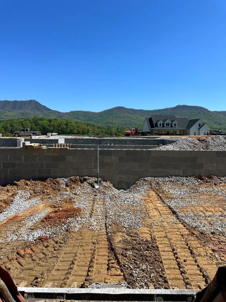A block foundation dug and backfilled with gravel, with a forested mountain ridge and blue sky behind