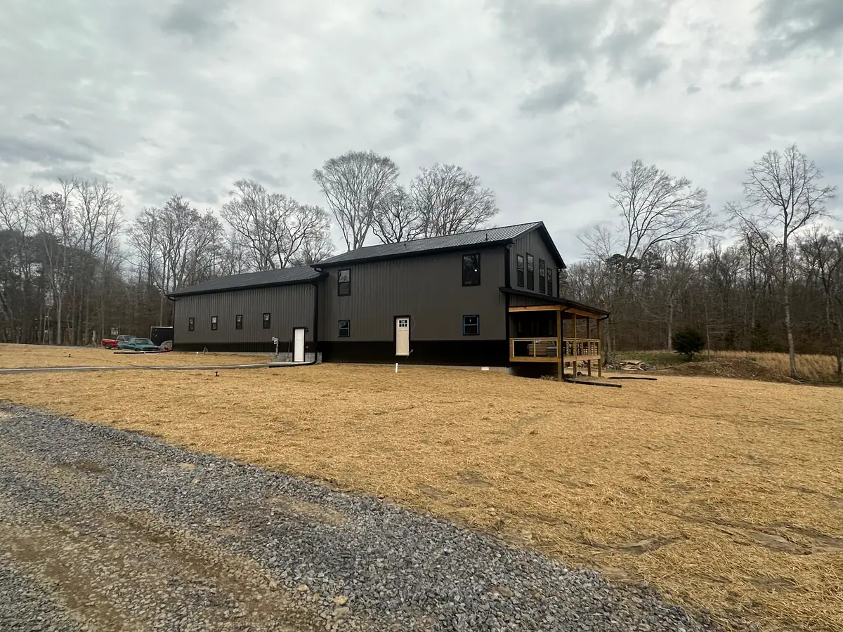 A wide view of a finished house site with a graded yard, gravel driveway and tree line behind