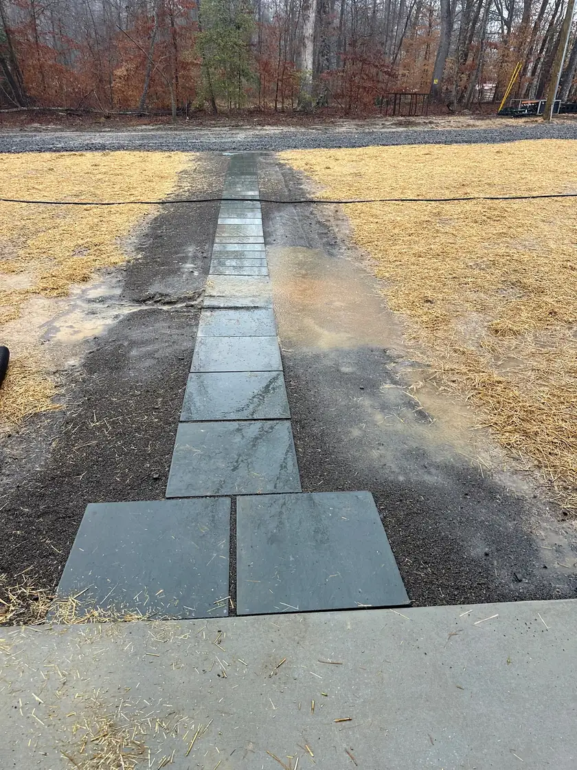 A stone-paver walkway leading across freshly strawed, graded ground toward a new home